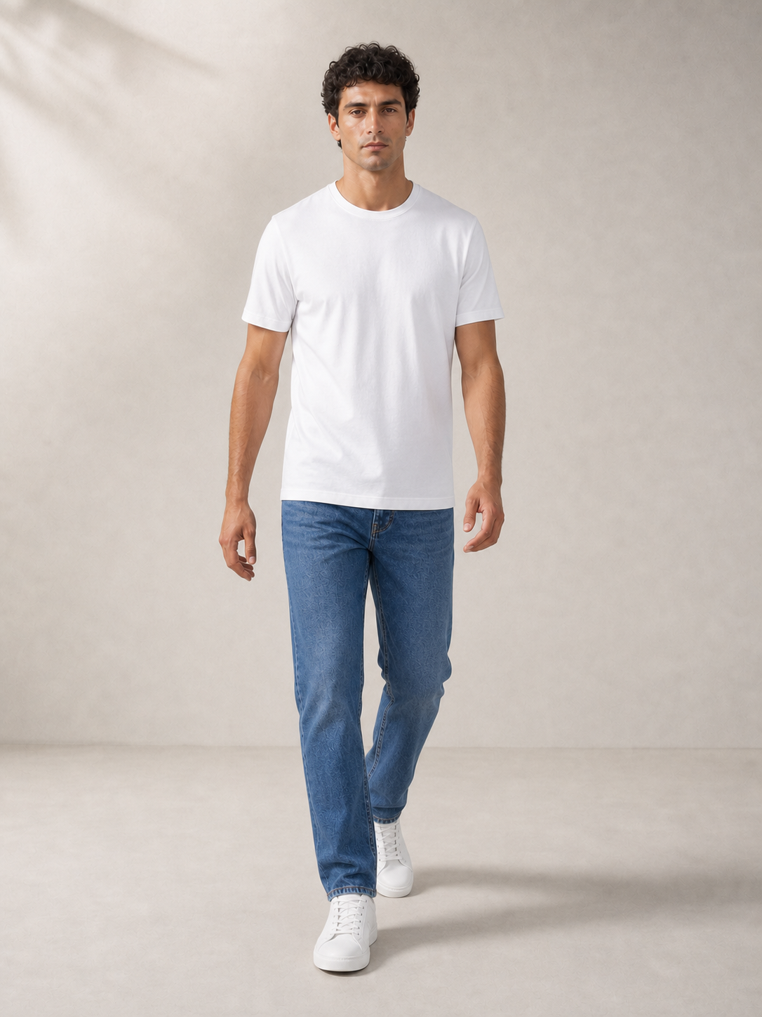 UOMO Essential White Tee on a walking male model in blue jeans and white sneakers