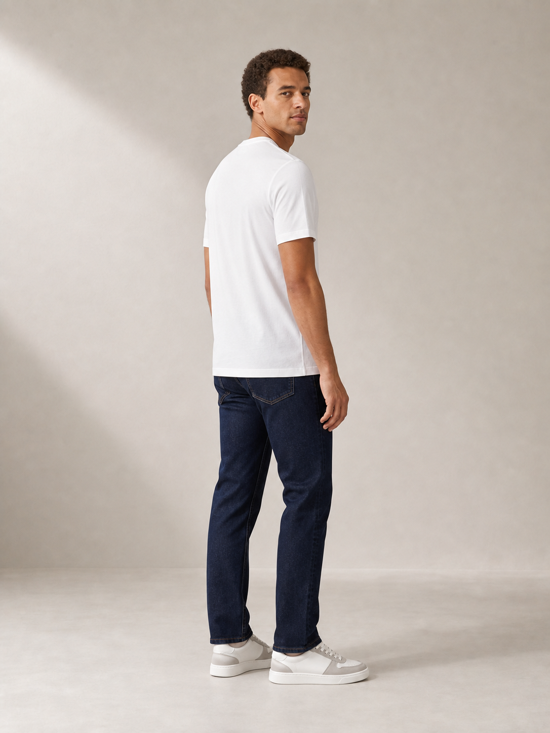 UOMO Fine White Tee rear three-quarter view on a male model in dark indigo jeans and grey-white sneakers