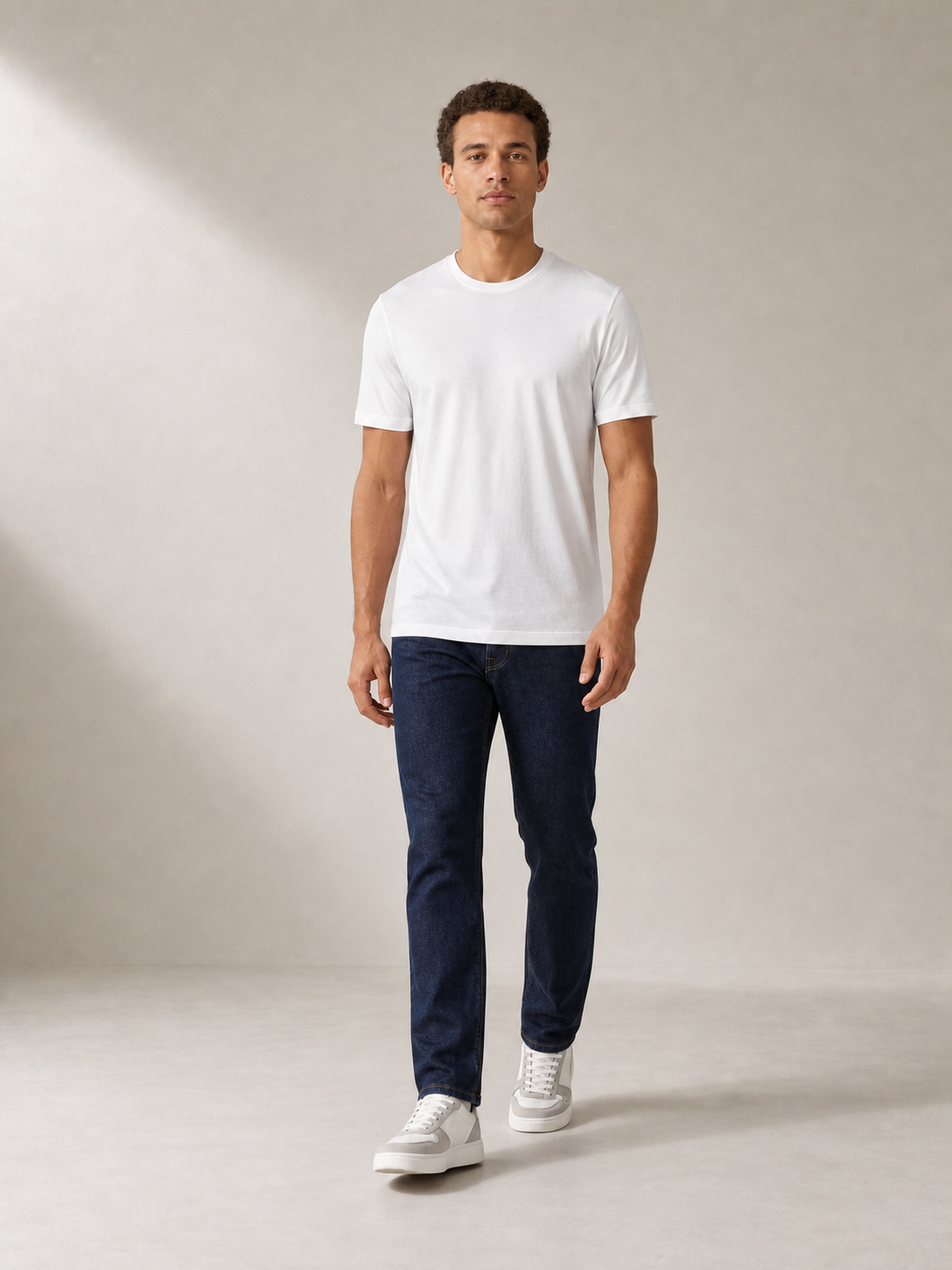 UOMO Fine White Tee on a walking male model in dark indigo jeans and grey-white sneakers